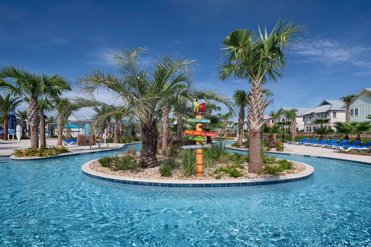 A tropical-style lazy river winds through lush palm trees, with blue lounge chairs lining the poolside and a whimsical signpost with parrots adding a playful touch. The water slides are visible in the distance, and families float happily in the water.